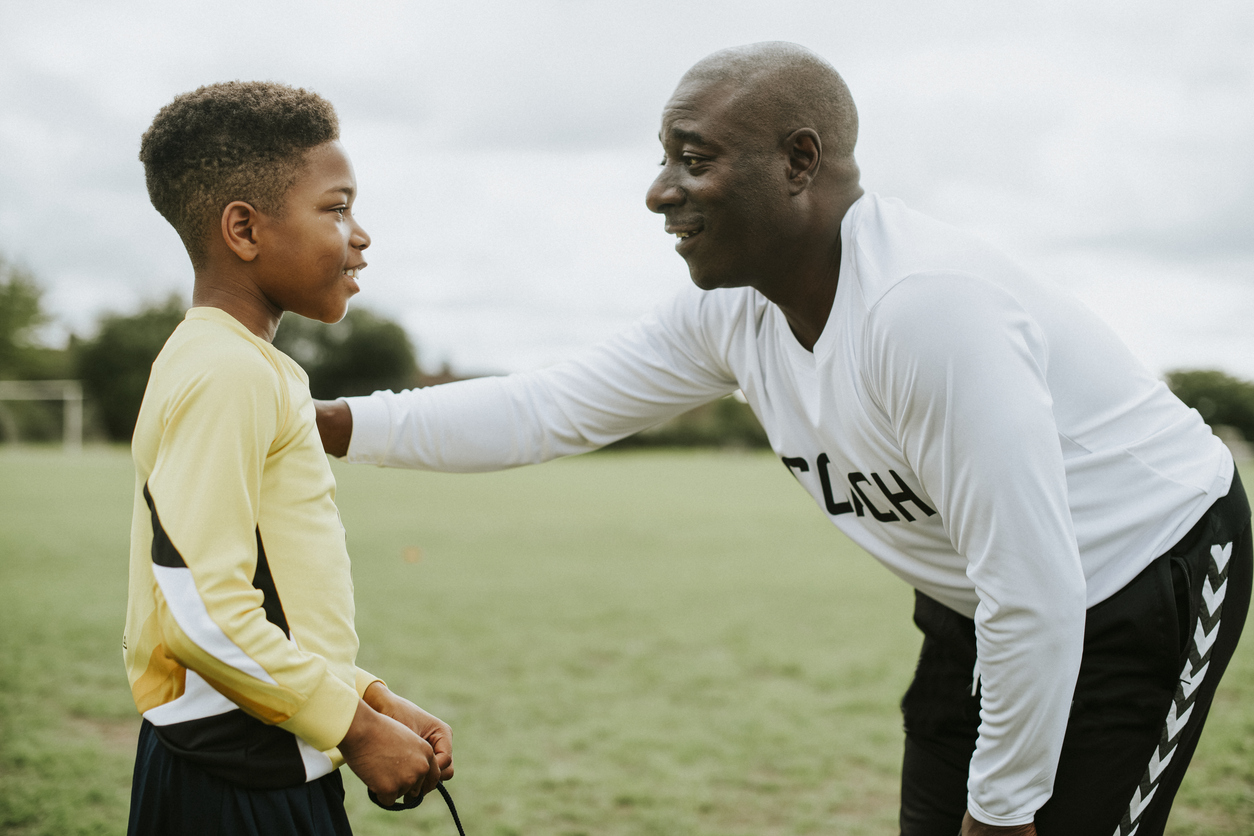 Mature African American football coach advising kid.